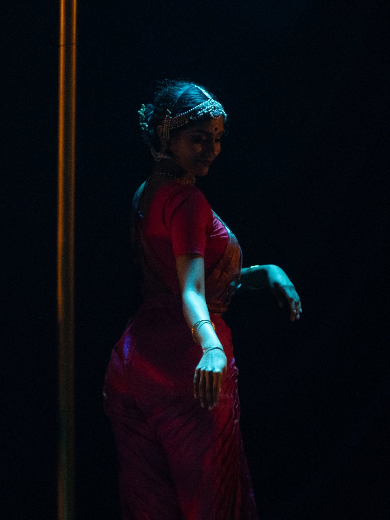 Classical dancer in a crimson saree, glancing down in soft stage light